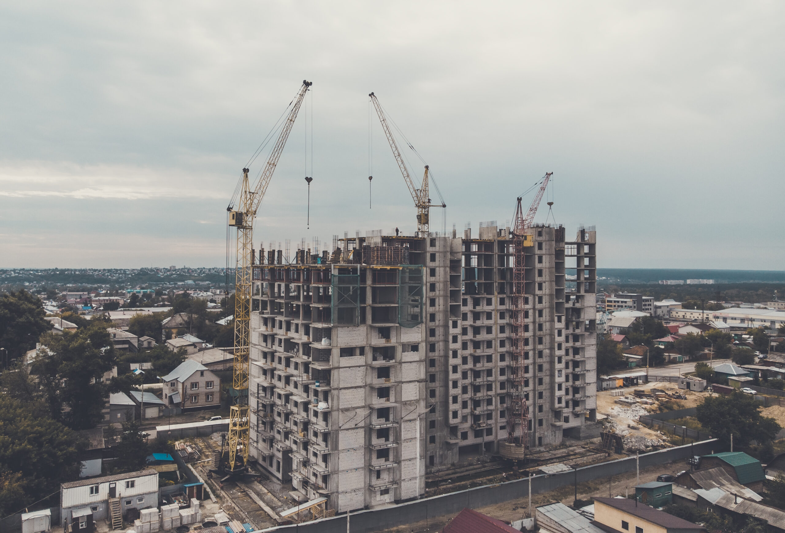 A new block of flats is erected in a low-rize houses town area. Process of housing. Town housing development problems. Large-sized prefabricated blocks in housing erection. A freezed building project